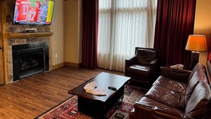 Una sala de estar con chimenea de piedra, un televisor montado encima, un sofá de cuero, una mesa de centro y una lámpara.
