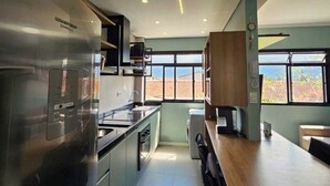 A modern kitchen with a stainless steel refrigerator, a wooden countertop, and a view of the cityscape through large windows.