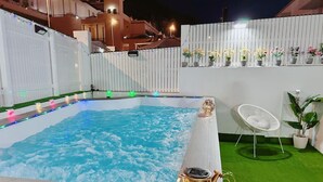 Banyera d'hidromassatge amb vora de fusta, envoltada per una tanca blanca, una cadira blanca i plantes en testos.