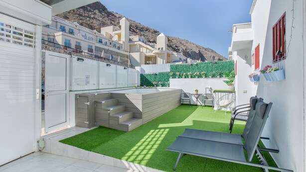 Un pati exterior modern amb gespa artificial, zona de seients i piscina.