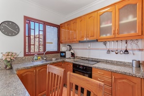 A kitchen with wooden cabinets, granite countertops, a clock, and a window with a view.