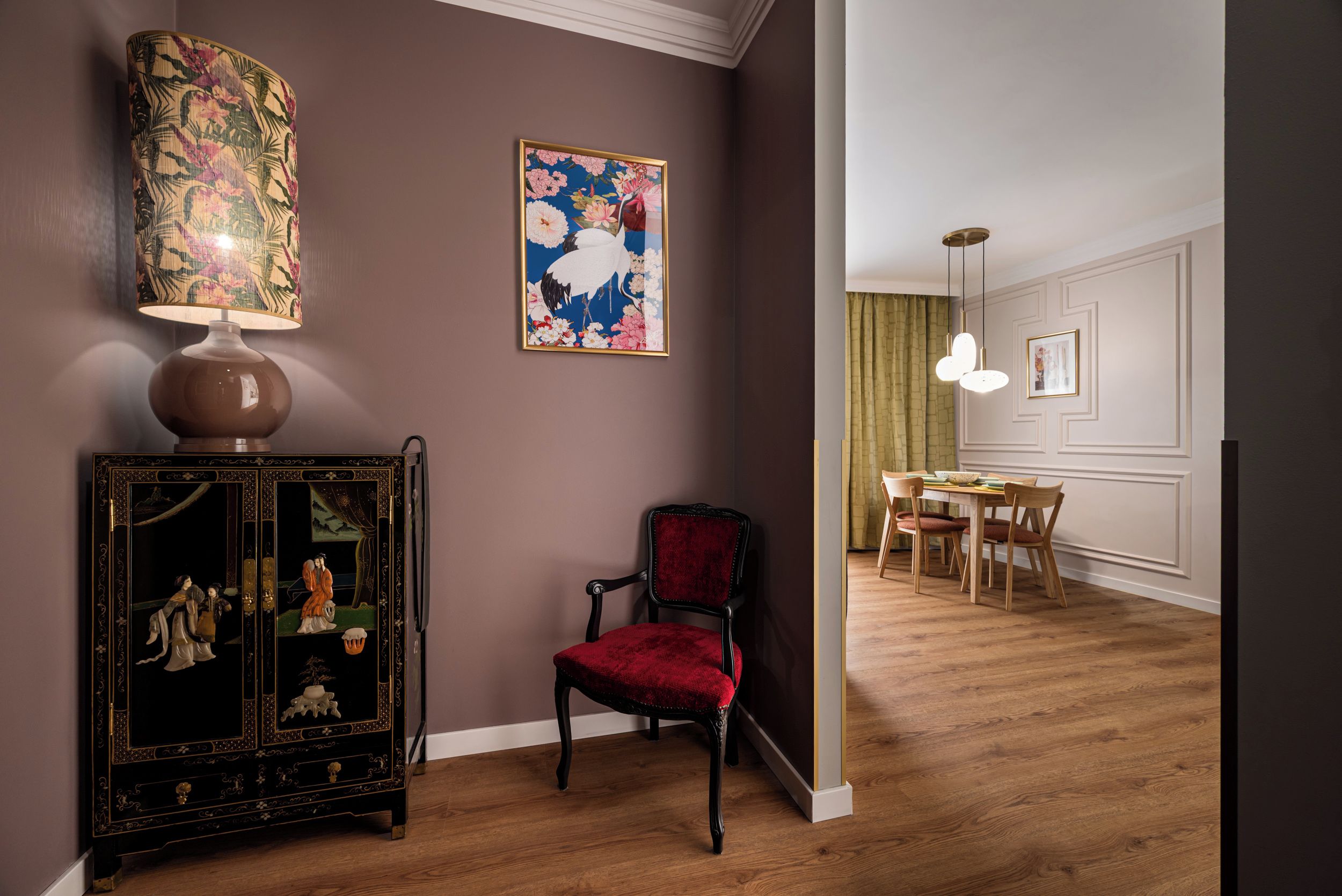 A room with a dark wall, a traditional cabinet with intricate designs, a red chair, and a dining area with a table and chairs.
