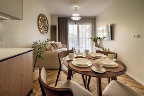 Uma sala de jantar moderna com uma mesa redonda posta para quatro pessoas, um sofá e uma janela grande com cortinas.