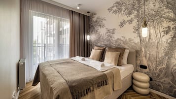 A hotel room with a large bed, a radiator, a window with sheer curtains, and a wall with a nature-themed wallpaper.