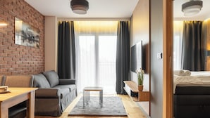 A modern hotel room with a brick accent wall, a sofa, a small table, a TV, and a bed. - RentPlanet - Sienkiewicza Residence (Wrocław)