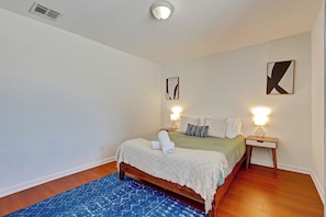 Een slaapkamer met een bed, nachtlampjes, een blauw vloerkleed en twee wanddecoraties.