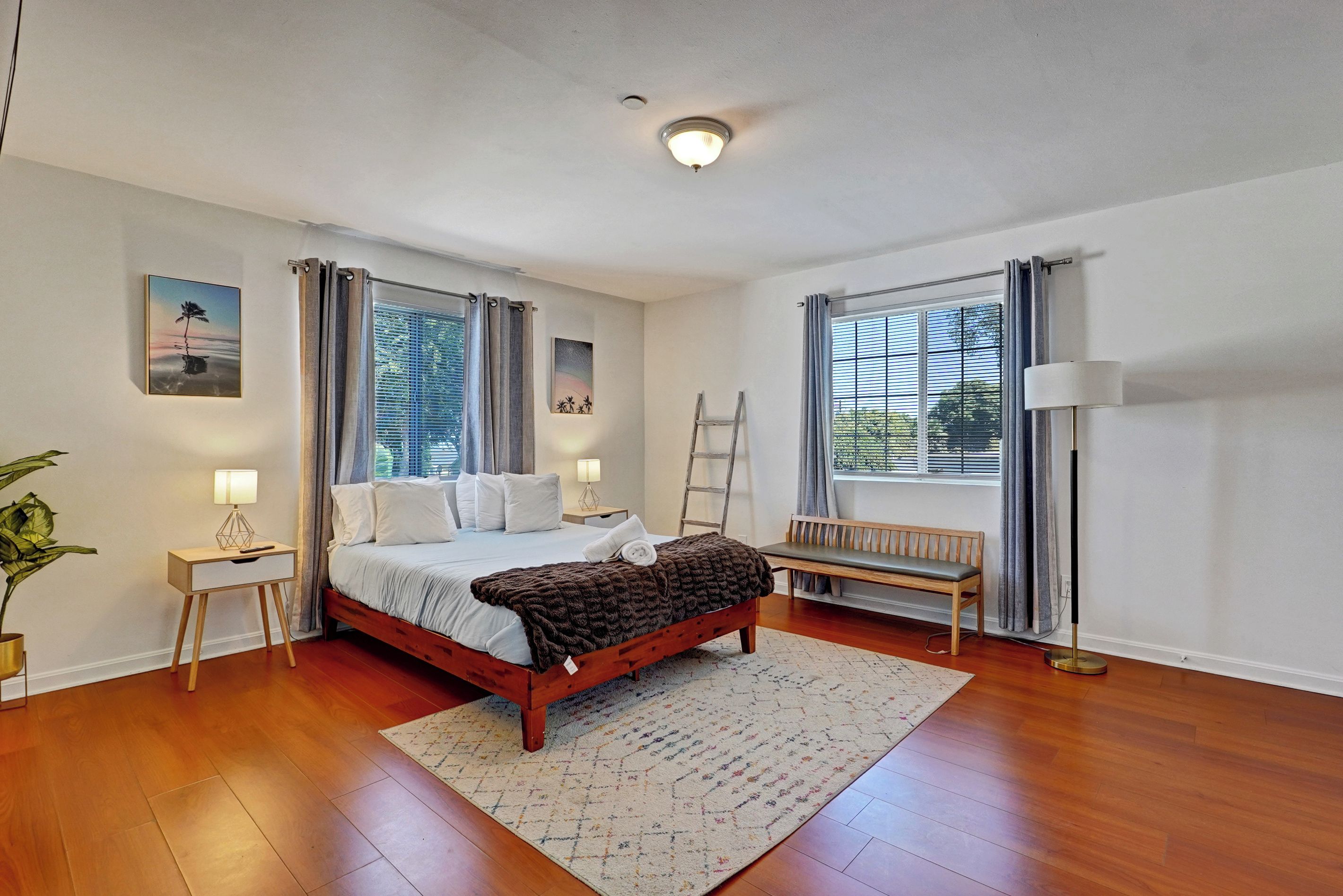 A well-lit bedroom with a wooden bed, a bench, a desk, and a floor lamp.