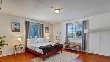 A well-lit bedroom with a wooden bed, a bench, a desk, and a floor lamp.
