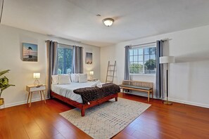 A well-lit bedroom with a wooden bed, a bench, a desk, and a floor lamp. - 4BR by Amazon & Sony Studios | Walk to Downtown (Culver City)