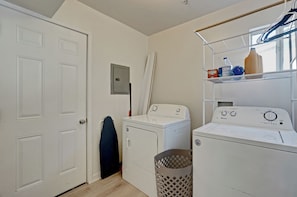 A laundry room with two washing machines, a dryer, a utility room door, and a laundry basket.
