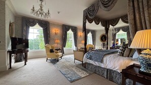 A spacious bedroom with a large bed, a sitting area with a chair and a table, a television, and a chandelier. - Park Hall Manor (High Peak)