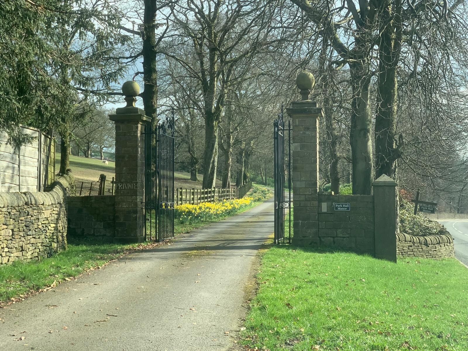 A pathway leading to a gated entrance with stone walls and a sign indicating 'Park Hall Manor'.