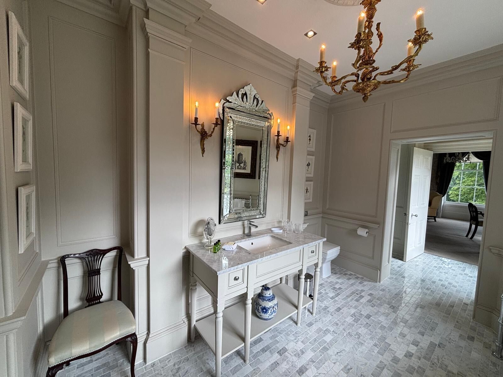 A spacious bathroom with a large mirror, white vanity, and a chandelier.