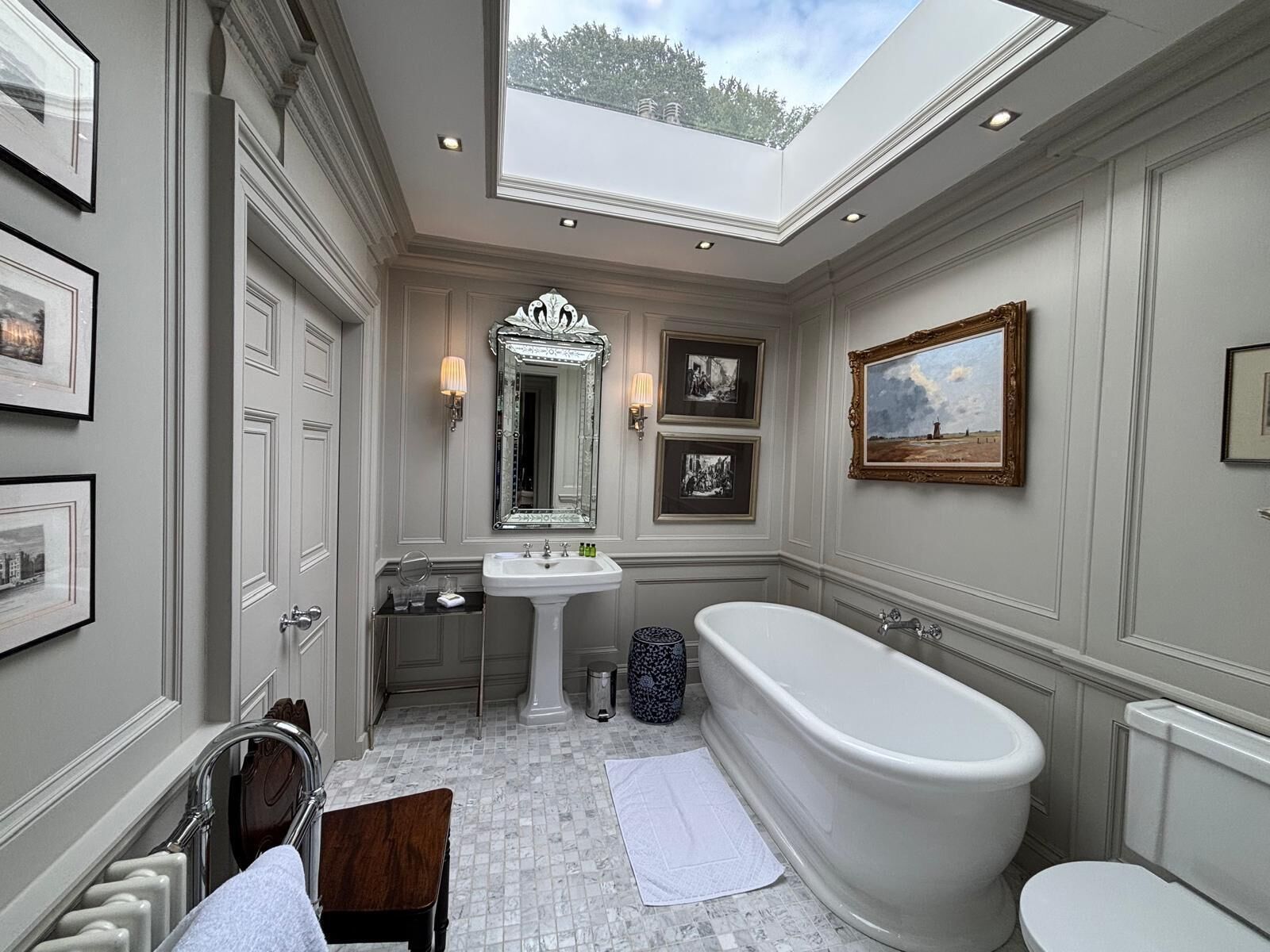 A classic bathroom with a freestanding bathtub, a large mirror, and framed pictures on the walls.