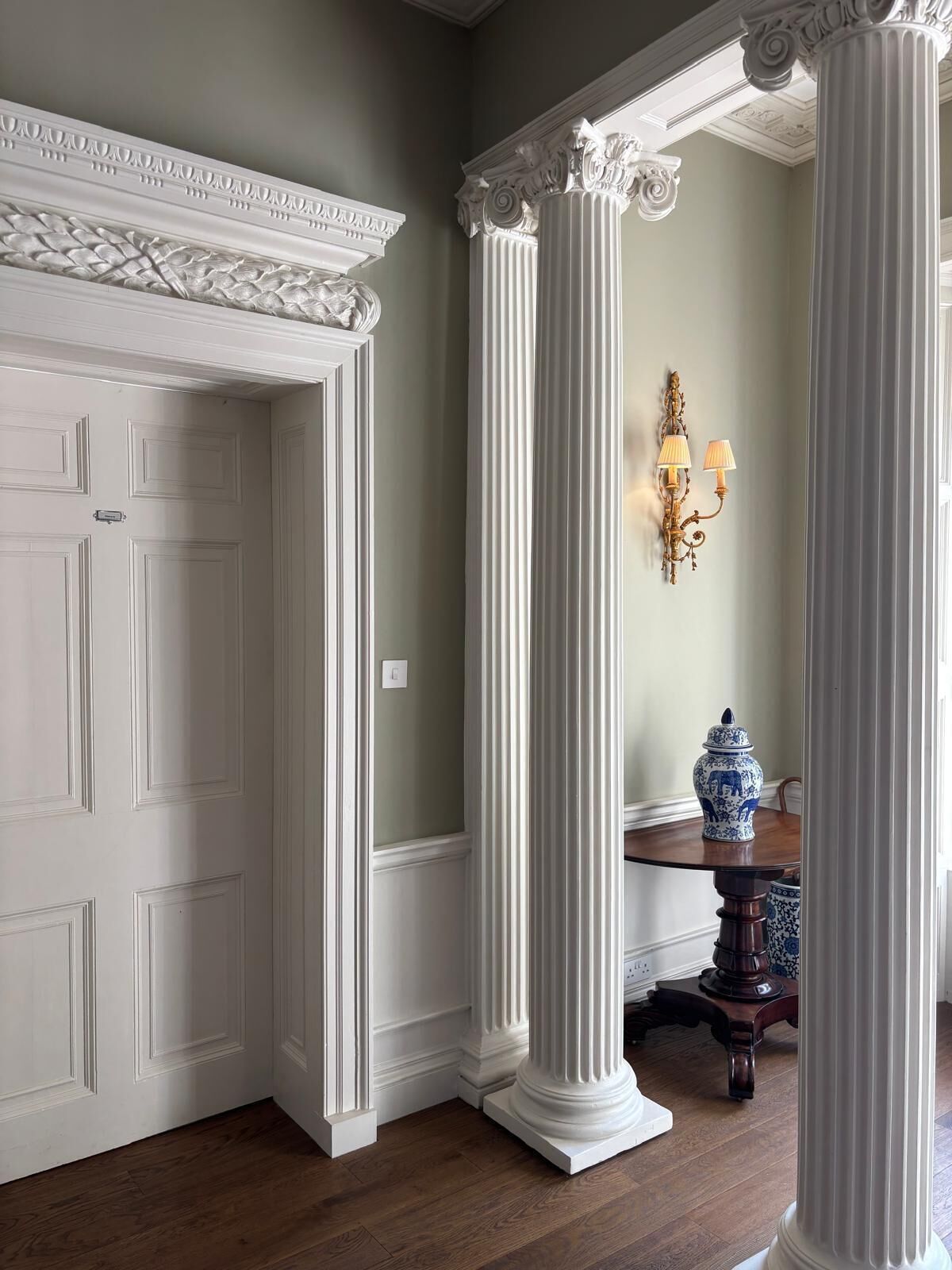 A room with a white door, a white fireplace, and a table with a blue vase.