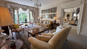 A spacious living room with a large window, elegant furniture, and a chandelier. - Park Hall Manor (High Peak)