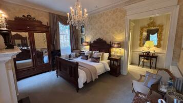 Un espacioso dormitorio con una cama grande, un candelabro, un espejo y una zona de estar con una mesa y sillas.