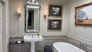 Un baño clásico con lavamanos pedestal, una bañera independiente y dos fotografías en blanco y negro enmarcadas en la pared.