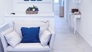 Een moderne woonkamer met een witte bank, een blauw kussen en een rieten mand met planten op een witte console tafel.