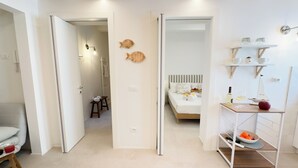 A modern hotel room with a bed, a small table with a bottle and glasses, and a shelf with jars and a toy sailboat. - Calle Piva, 788 by Ca-Sa Check (Chioggia)