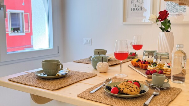 Une table mise pour le petit-déjeuner, avec une nappe pour deux personnes, comprenant des assiettes de biscuits et de fruits rouges, des verres de jus rouge et un vase avec une rose rouge.