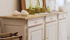Un meuble blanc en bois avec un miroir, des bouteilles en verre vert et une lampe.