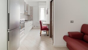 A modern kitchen with stainless steel appliances, a dining area with a red chair, and a red sofa.