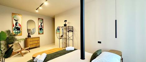 Une chambre à coucher moderne avec un grand lit, une commode en bois, un miroir et deux œuvres d’art accrochées au mur.