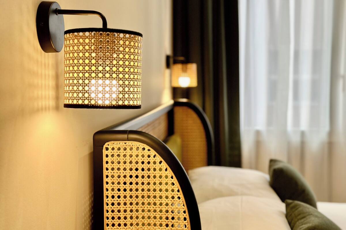 Une lampe murale au design perforé, une tête de lit incurvée et un lit avec des oreillers.