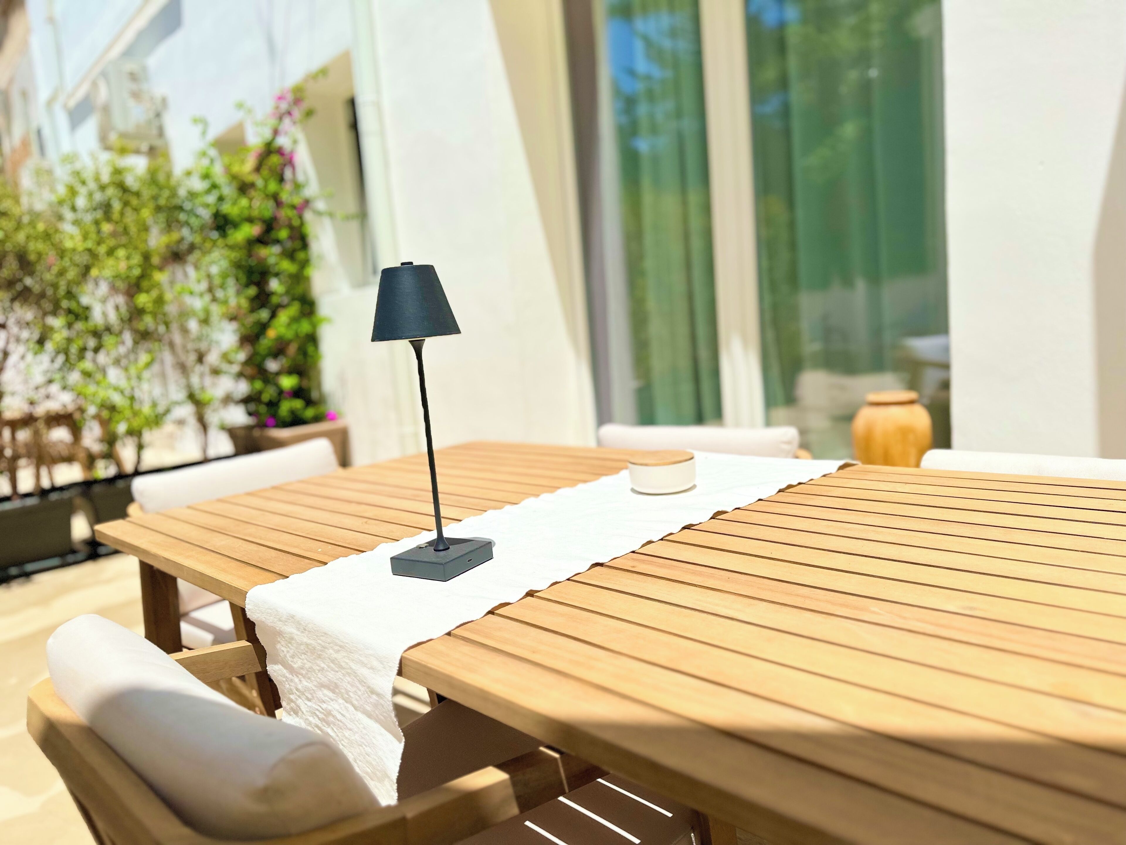 A wooden table with a white cloth, a black lamp, and a white cushion.