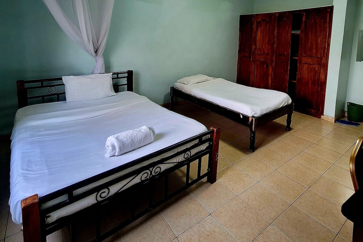 A room with two beds, a wooden wardrobe, and a ceiling light.