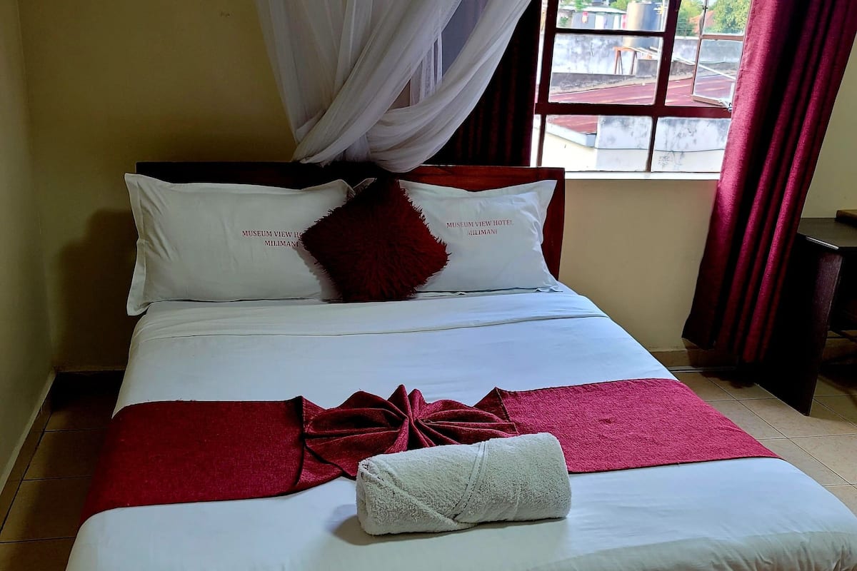 A neatly made bed with white and red bedding, a red throw blanket, and a white towel.