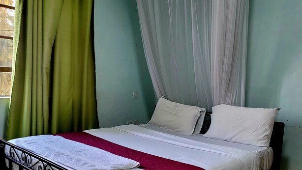 Ein Bett mit weißer Matratze und Kissen, einer roten Decke und einem grünen Vorhang.
