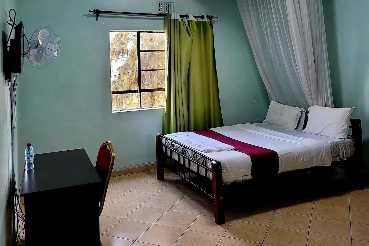 A bedroom with a bed, a desk, a chair, a window with curtains, and a ceiling fan.