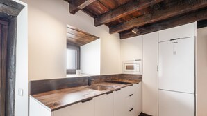 Une cuisine avec des meubles blancs, un plan de travail en bois, un four à micro-ondes encastré et un réfrigérateur blanc.