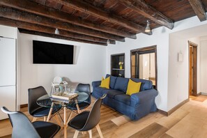 A modern living room with a wooden ceiling, a blue sofa with yellow cushions, a glass dining table with chairs, and a flat-screen TV mounted on the wall. - Vacation at 'Casa Miranda 3' with Private Terrace, Wi-Fi and Air Conditioning (Igueste de Candelaria)