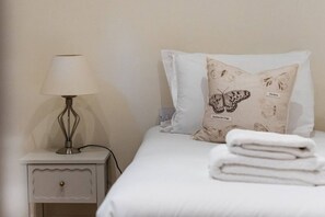 A neatly made bed with a pillow featuring a butterfly design, a bedside lamp, and a folded towel on a white nightstand.