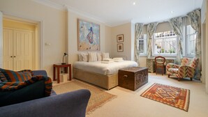 A well-lit bedroom with a large bed, a desk, a chair, and a colorful rug.
