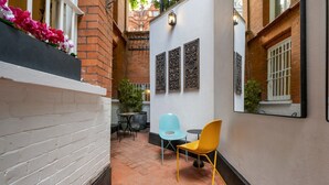 A narrow courtyard with a white brick wall, a yellow chair, a blue chair, and a small table.