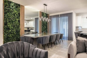 Una cocina moderna con una isla central, sillas de tonos oscuros y una pared vertical con jardín.
