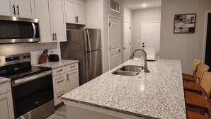 A modern kitchen with white cabinetry, stainless steel appliances, a granite countertop, and a built-in sink. - Landing | Stunning 2BD, Pool, Gym (Newberry)