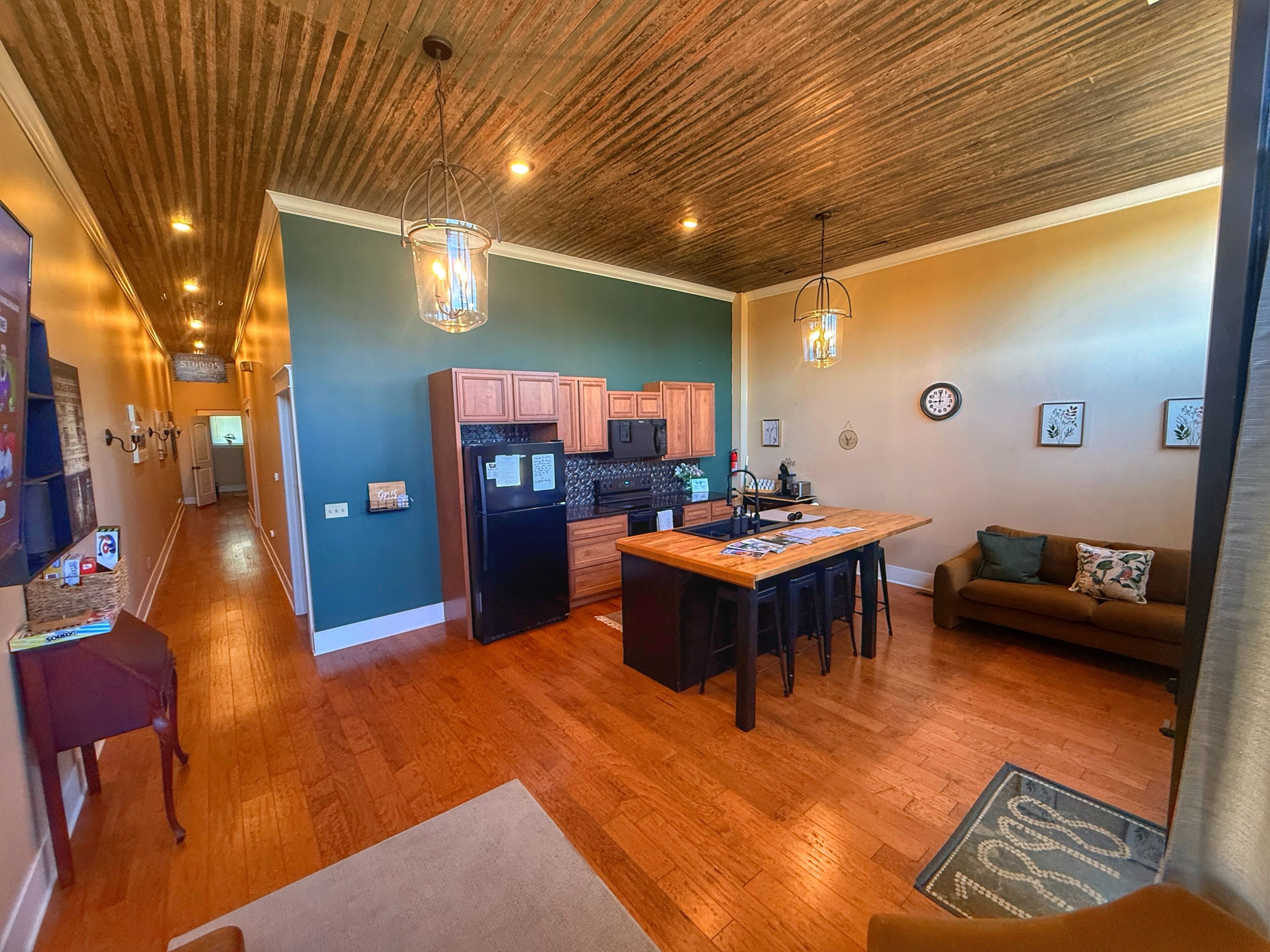 A modern kitchen with wooden cabinets, a black refrigerator, and a dining area with a wooden table and chairs.