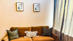 A living room with a brown sofa, two framed botanical prints on the wall, and a window with sheer curtains. - Stunning 2 bedroom in town, close to Shawnee National Forest (Jonesboro)