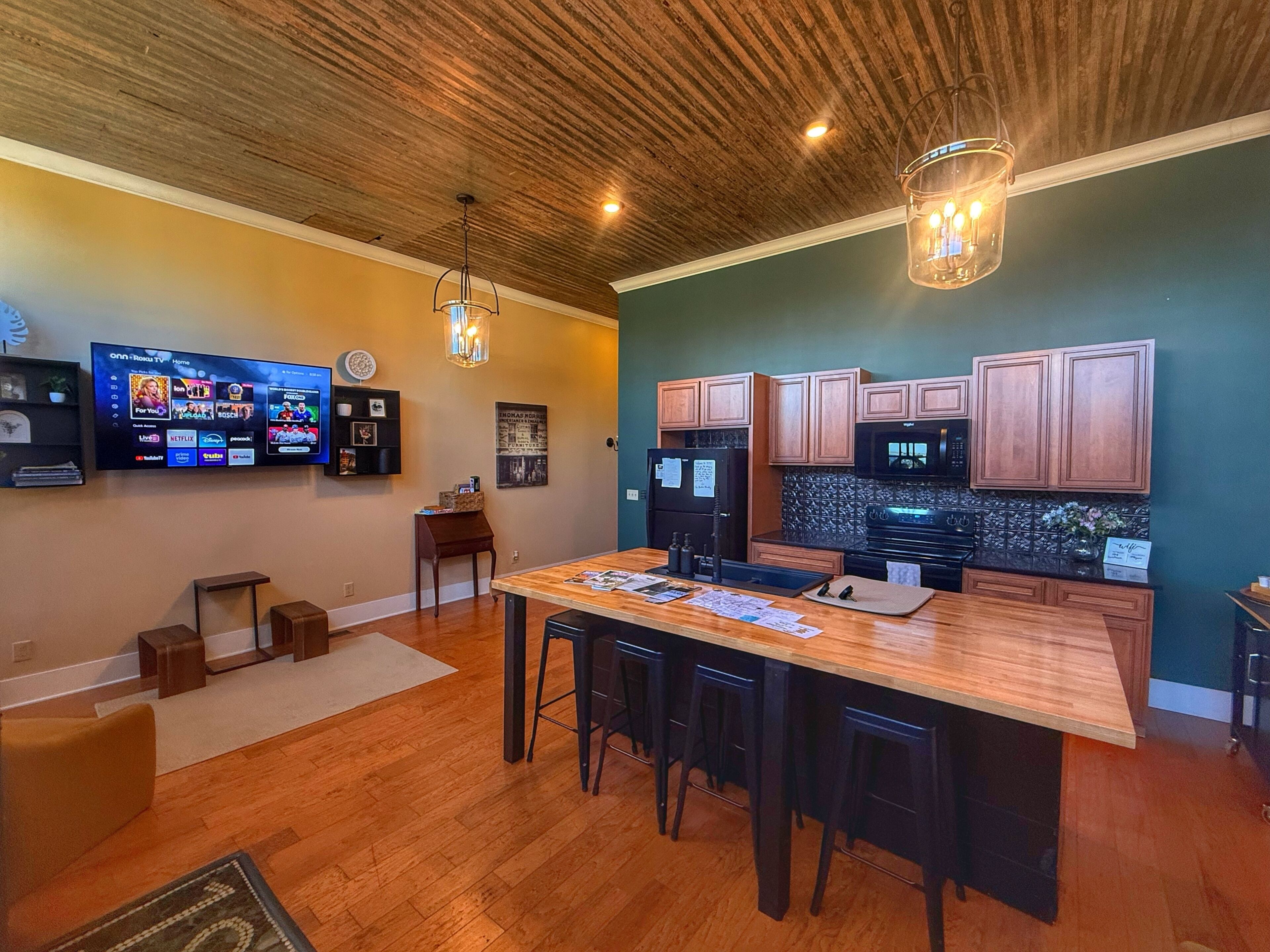 Una cocina moderna con armarios de madera, una isla central con taburetes de bar, un horno empotrado y un televisor montado en la pared.