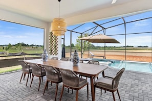 Un comedor con mesa de madera y sillas de mimbre, un jarrón grande y vista a una piscina.