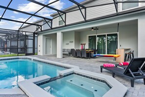 Uma área de piscina com hidromassagem, espreguiçadeiras e um alpendre coberto com mobiliário para áreas externas.
