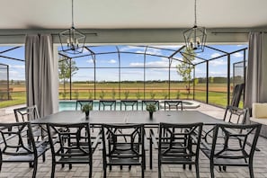 Un patio cubierto con piscina, mobiliario exterior y vistas al campo.