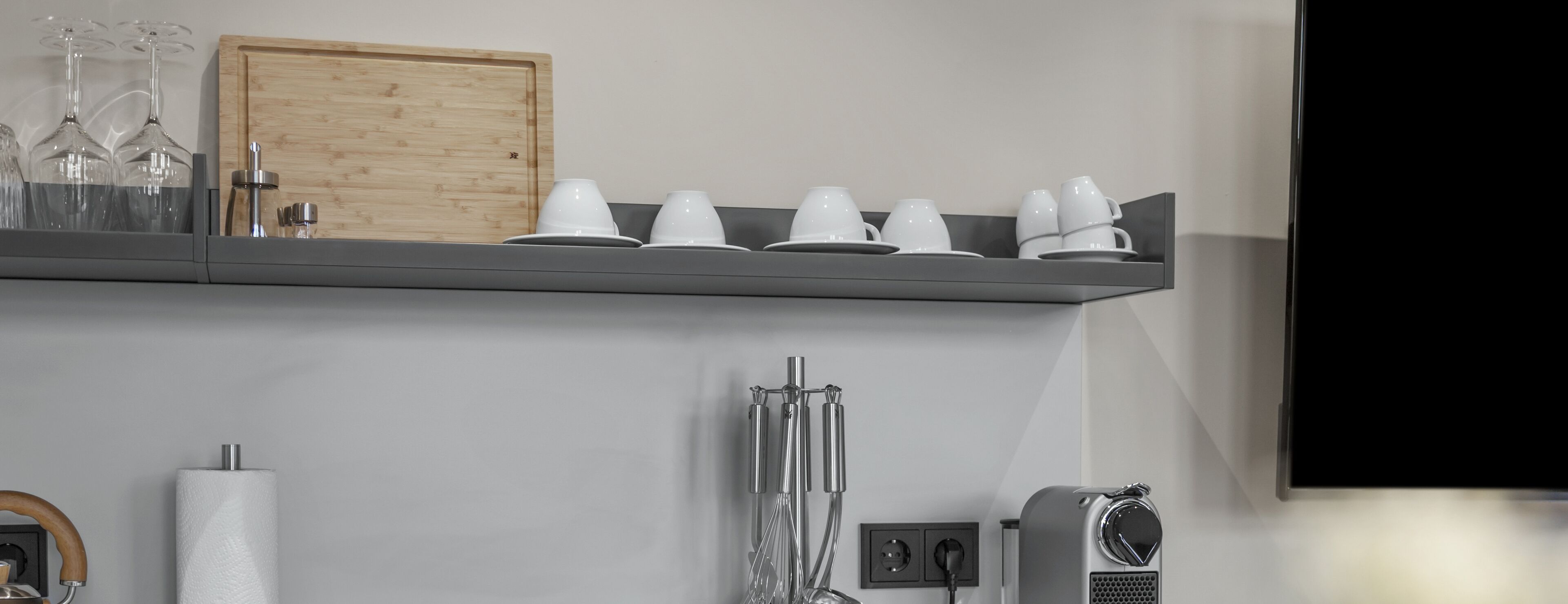 Eine Küche mit einem Holzkasten, einem Regal mit weißen Tassen und Gläsern, einem Papierhandtuchhalter und einer Kaffeemaschine.