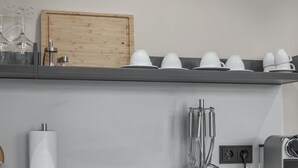 A kitchen with a wooden cabinet, a shelf with white cups and glasses, a paper towel holder, and a coffee machine. - City view apartment 9 Schlehe (Lüneburg)