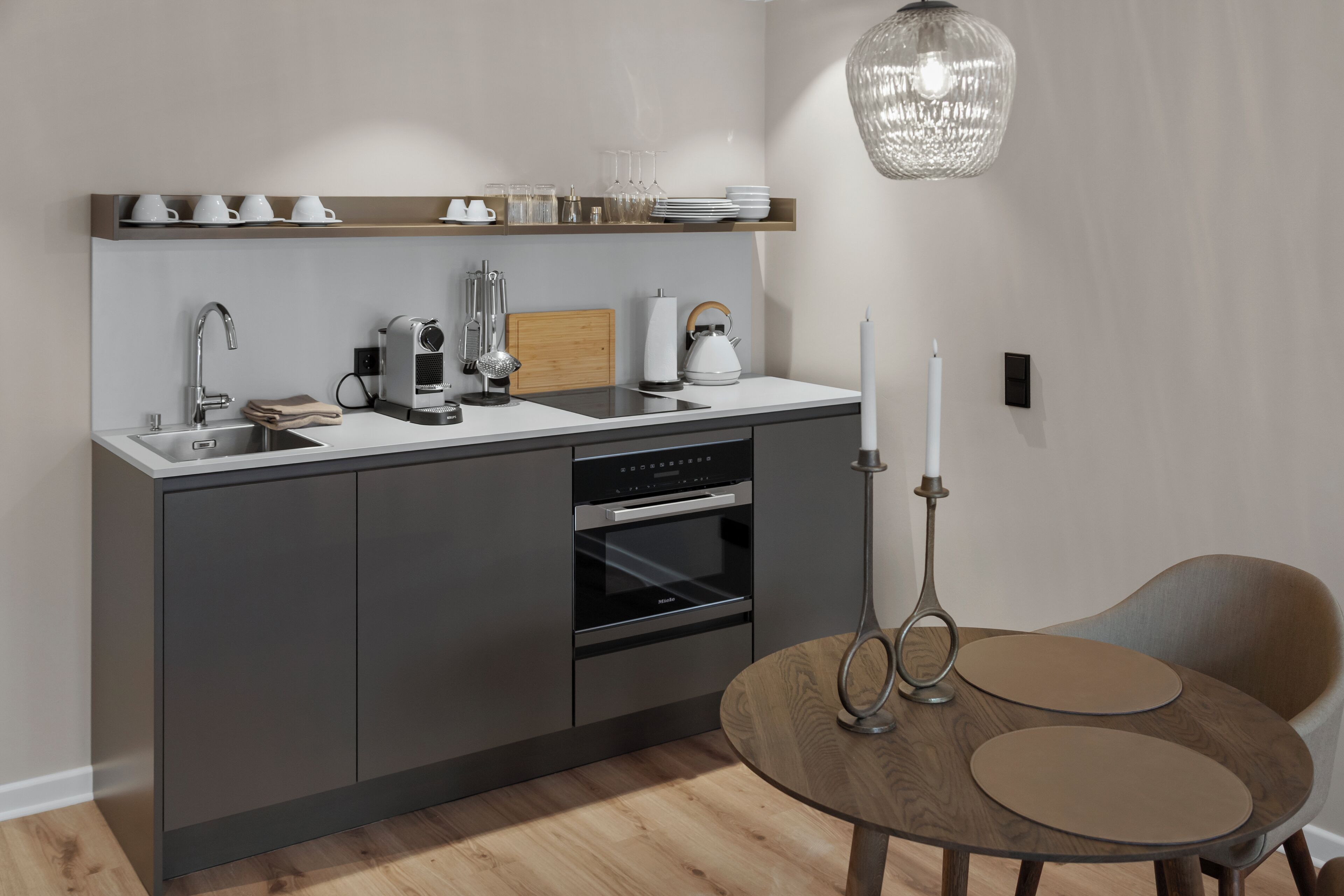 Una cocina moderna con horno empotrado, pileta y encimera de madera. Hay una mesa redonda con dos sillas y un candelabro.
